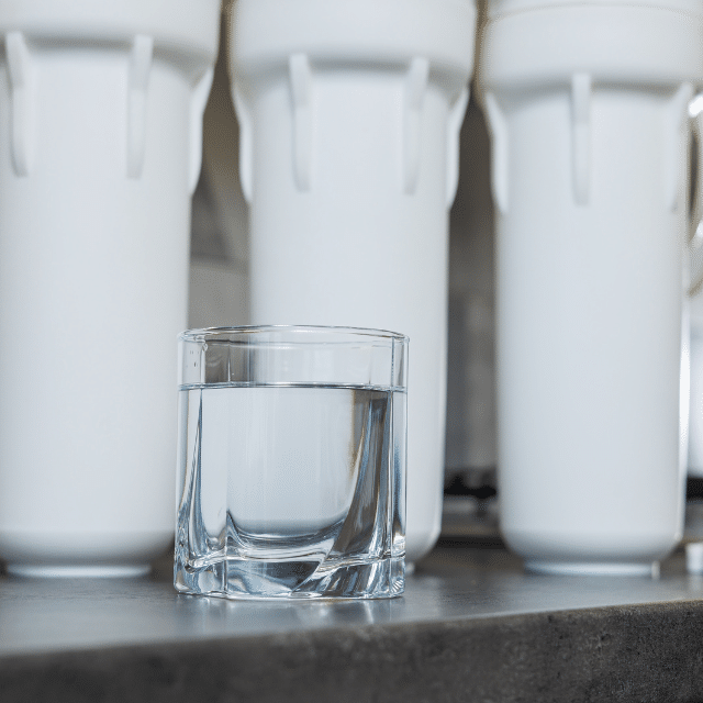 A glass of filtered water. Water filtration system with replaceable cartridges. A system in the apartment with three tanks for cleaning tap water.