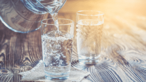 Versement d'eau dans un verre en verre sur une table en bois, avec un second verre d'eau en arrière-plan.