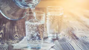 Versement d'eau dans un verre en verre sur une table en bois, avec un second verre d'eau en arrière-plan.