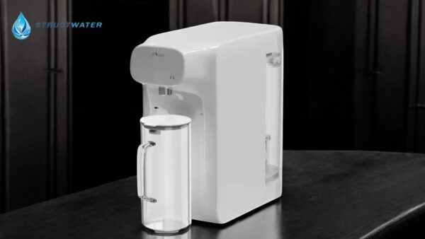 Mini Water reverse osmosis fountain from StructWater with empty carafe, set on a dark surface.